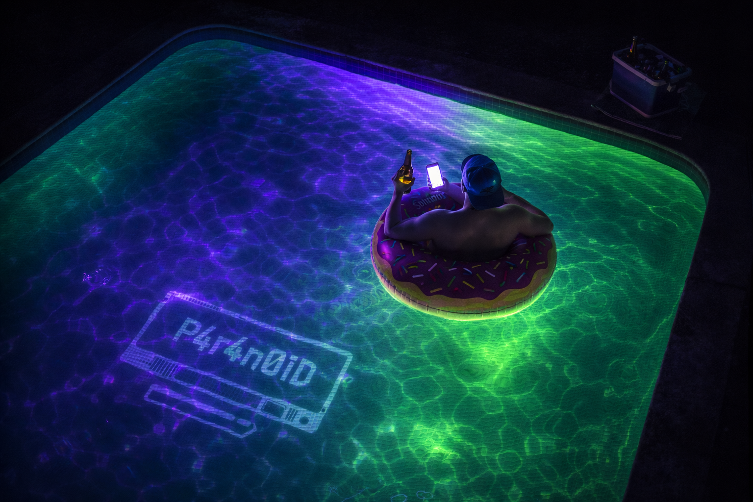 A man in a backwards ball cap floating in a donut pool float at night, beer in one hand and phone in the other, in a pool glowing acid green and purple with a P4r4n0iD retro terminal logo on the pool floor. Ice bucket poolside. Pitch darkness beyond the edges.